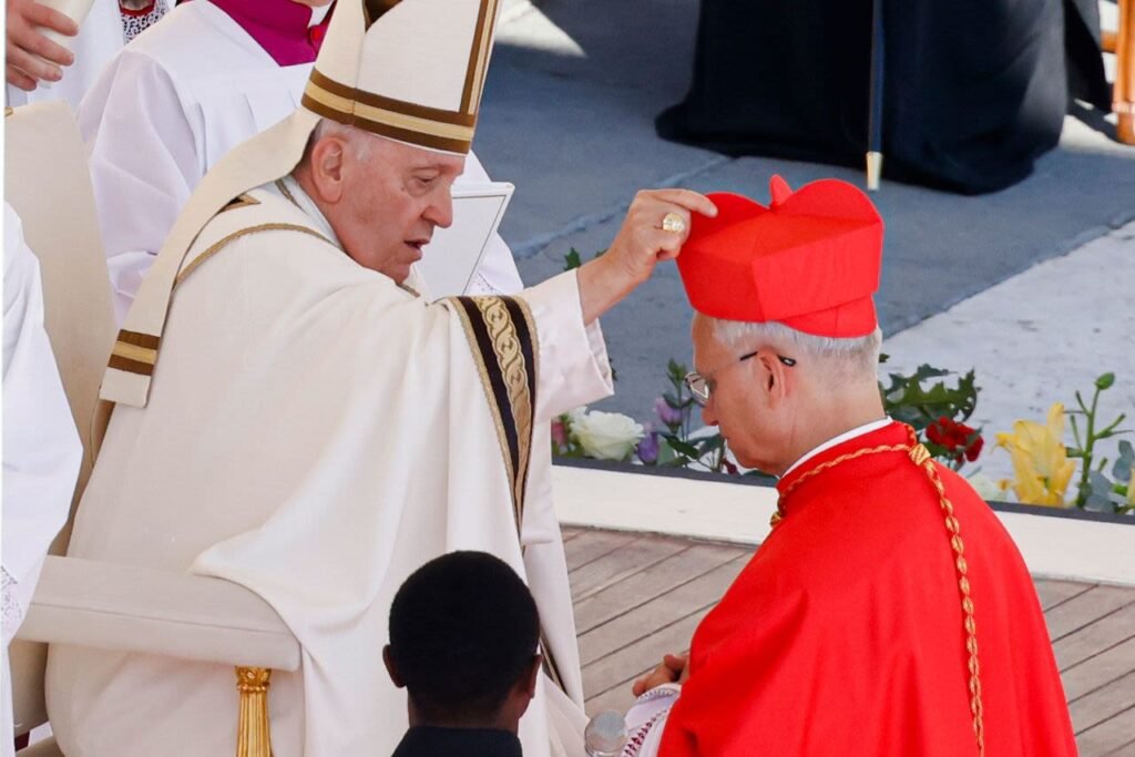 El Papa Francisco ajustando el solideo rojo de un cardenal arrodillado durante una ceremonia al aire libre.
Primer plano del Papa Francisco corrigiendo el zucchetto de un cardenal vestido de rojo.
Escena de una ceremonia religiosa con el Papa Francisco y un cardenal arrodillado.
El Santo Padre interactuando con un cardenal durante un evento público.
Fotografía del Papa Francisco y un cardenal en vestimentas litúrgicas en una ceremonia al aire libre.