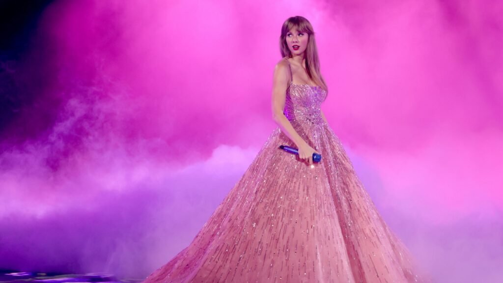 Taylor Swift con un vestido largo rosa y dorado brillante actuando en el "The Eras Tour".
Taylor Swift en el escenario con un vestido espectacular bajo luces rosas y humo.
La cantante Taylor Swift con un elegante vestido rosa y dorado durante un concierto.
Imagen de Taylor Swift durante su gira "The Eras Tour" con un vestido brillante.
Taylor Swift deslumbrando en el escenario con un vestido de ensueño rosa y dorado.